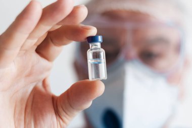 Coronavirus Covid-19 konsepti. Gözlüklü doktor ve koruma amaçlı solunum maskesi aşı şişesi tutuyor. Wuhan, Çin salgını Cov-19 belirtileri karantina arka planı Corona virüsü salgını.
