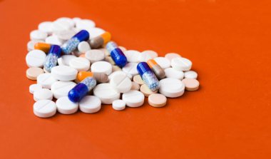 Beyaz haplar, kalp şeklinde haplar, kırmızı turuncu arka planda kapsüller. Fotokopi alanı ile tedavi tedavisi için ilaç reçetesi