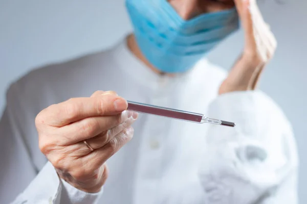 Coronavirus karantina ve hava kirliliği pm2.5 konsepti. Termometreyi korumak için solunum maskesi takan yaşlı hasta kadın. Wuhan, Çin salgını virüs belirtileri.