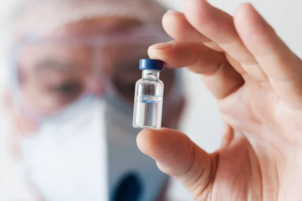 Coronavirus Covid-19 konsepti. Gözlüklü doktor ve koruma amaçlı solunum maskesi aşı şişesi tutuyor. Wuhan, Çin salgını Cov-19 belirtileri karantina arka planı Corona virüsü salgını.