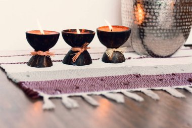 Konforlu ev dekorasyonu, hindistan cevizi kabuğunda yanan spa aromalı mumlar, çok renkli bir halı, metal vazonun yanında. 