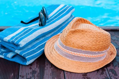Eski yaz hasır hasır hasır plaj şapkası, güneş gözlükleri ve yüzme havuzunun yanındaki mavi havlu, tropikal arka plan.