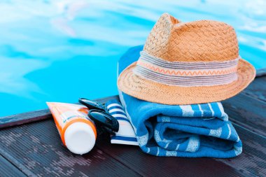 Eski yaz hasır hasır hasır plaj şapkası, güneş gözlüğü, güneş kremi tüpü ve yüzme havuzunun yanındaki mavi havlu, tropikal arka plan.