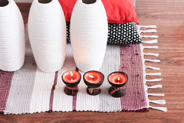 Cozy home interior decor, burning spa aroma candles in coconut shell on a multi-colored rug, near white vase and decorative pillows