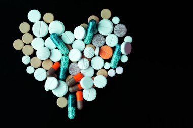 Kalp şeklinde bir yığın renkli hap, siyah arka planda tabletler ve kapsüller. Tedavi için ilaç reçetesi sağlık hizmetleri konsepti, fotokopi alanı ile üst görünüm