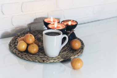 Hindistan cevizi kabuğunda yanan spa aromalı mumlar, bir fincan çay, hasır üzerinde mandalinalar cam beyaz masa üzerinde duruyor, rahat ev içi arka plan