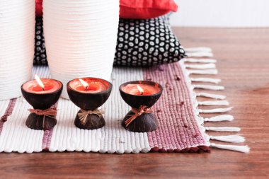 Konforlu ev dekorasyonu, hindistan cevizi kabuğunda yanan spa aromalı mumlar, çok renkli bir halı, beyaz vazo ve dekoratif yastıklar. 