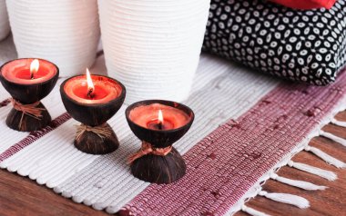 Konforlu ev dekorasyonu, hindistan cevizi kabuğunda yanan spa aromalı mumlar, çok renkli bir halı, beyaz vazo ve dekoratif yastıklar. 