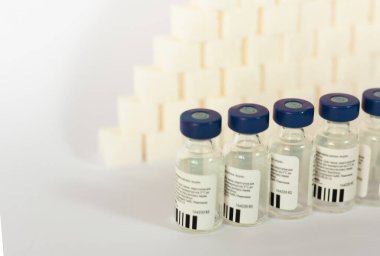 Şeker bağımlılığı, insülin direnci, sağlıksız beslenme, şeker küpleri piramidi, beyaz arka planda aşı için insülin şişeleri, diyabet korunması tıbbi konsept