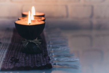 Hindistan cevizi kabuğunda yanan spa aromalı mumlar. Beyaz duvarın karşısında örülmüş çok renkli bir halı.
