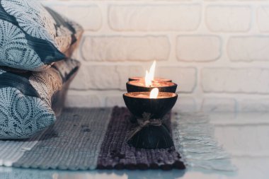 Hindistan cevizi kabuğunda yanan spa aromalı mum örülmüş çok renkli bir halı ve beyaz duvarın karşısındaki gri yastıklar, rahat ev içi.