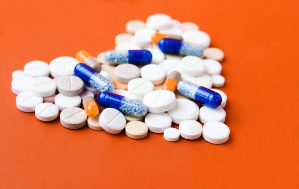 Heap of pills, tablets, capsules on red orange background. Drug prescription for treatment medication health care concept wth copy space