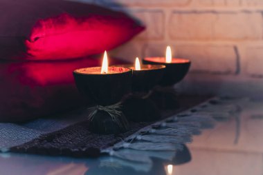 Hindistan cevizi kabuğunda yanan spa aroması mumu örülmüş çok renkli bir halı ve beyaz duvarın karşısında kırmızı yastıklar, rahat ev içi
