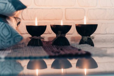 Hindistan cevizi kabuğunda yanan spa aromalı mum örülmüş çok renkli bir halı ve beyaz duvarın karşısındaki gri yastıklar, rahat ev içi.