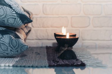 Hindistan cevizi kabuğunda yanan spa aromalı mum örülmüş çok renkli bir halı ve beyaz duvarın karşısındaki gri yastıklar, rahat ev içi.