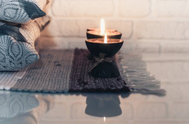 Hindistan cevizi kabuğunda yanan spa aromalı mum örülmüş çok renkli bir halı ve beyaz duvarın karşısındaki gri yastıklar, rahat ev içi.