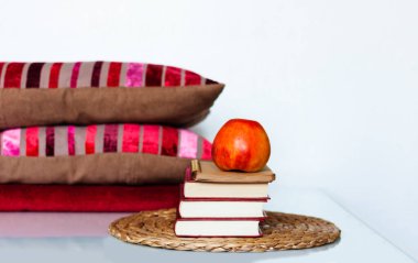 Konforlu ev dekorasyonu: Elma, kitap yığını, yastık ve ekose beyaz bir masa. Uzaktan eğitim. Karantina konsepti: