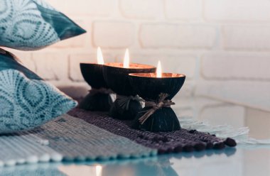 Hindistan cevizi kabuğunda yanan spa aromalı mum örülmüş çok renkli bir halı ve beyaz duvarın karşısındaki gri yastıklar, rahat ev içi.
