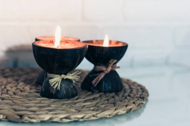 Hindistan cevizi kabuğunda yanan spa aromalı mumlar hasır üzerinde cam beyaz bir masa üzerinde duruyor, rahat ev içi arka plan
