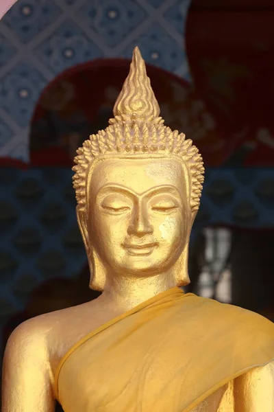 Close up of the face of a golden Buddha sculpture adorned in an orange robe