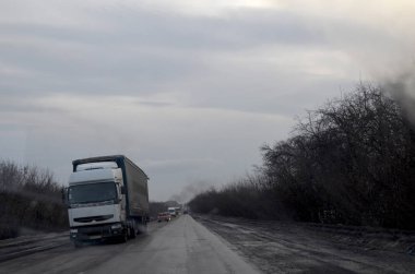Sıkıcı havada kamyonet yolda. Kamyon ve arabalar kış-sonbahar sezonunda yolda ilerliyorlar. Yol trafiği. Hayat yollarda. Kışın arabayla seyahat etmek. Sonbaharda arabayla seyahat etmek. Malların nakliyesi. Kötü hava. Bulutlu bir gün.