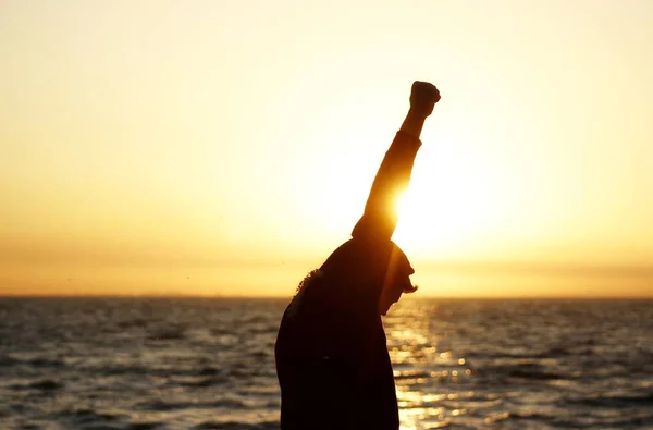bir kazanan yükseltilmiş bir el ile deniz ufku karşı poz gündoğumu arka plan üzerinde adam silüeti