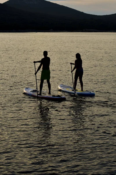 Couple is paddling on sup boards on the sea during sunset time