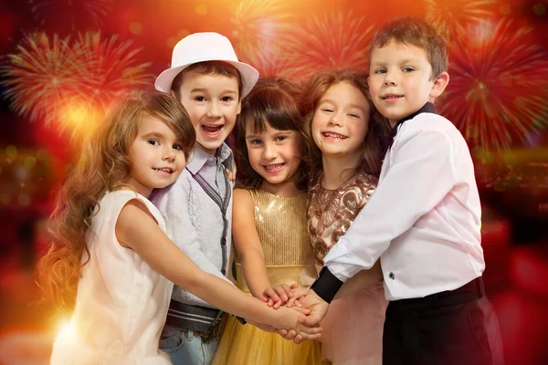 Group of happy kids in holiday clothes with fireworks background — Stock Photo, Image