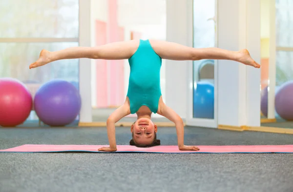 Flexible little girl gymnast standing on head in gym — Stockfoto