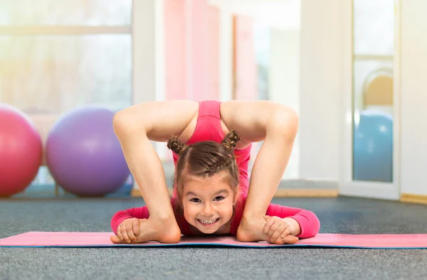 Niña gimnasta flexible haciendo ejercicio acrobático en el gimnasio —  Fotos de Stock