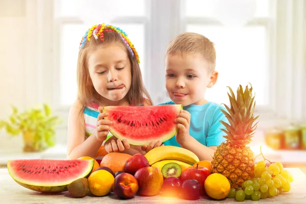 Happy kids eating watermelon with fruits in kitchen — Stock Photo, Image