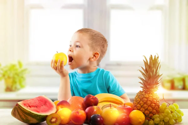 Little boy eating apple with fruits in kitchen — Stock Photo, Image