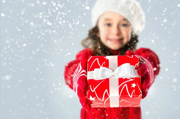 Lycklig liten flicka med julklapp på snö bakgrund — Stockfoto