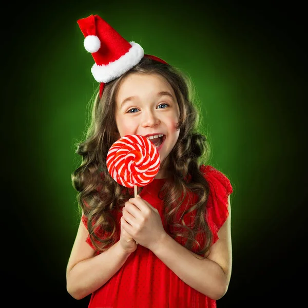 Niña sonriente en sombrero de santas con caramelo, fondo verde aislado —  Fotos de Stock