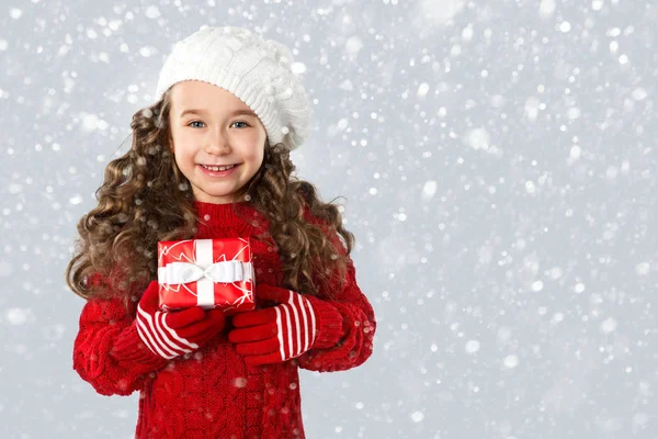 Fashion little girl with Christmas gift, on snow background — Stock Photo, Image