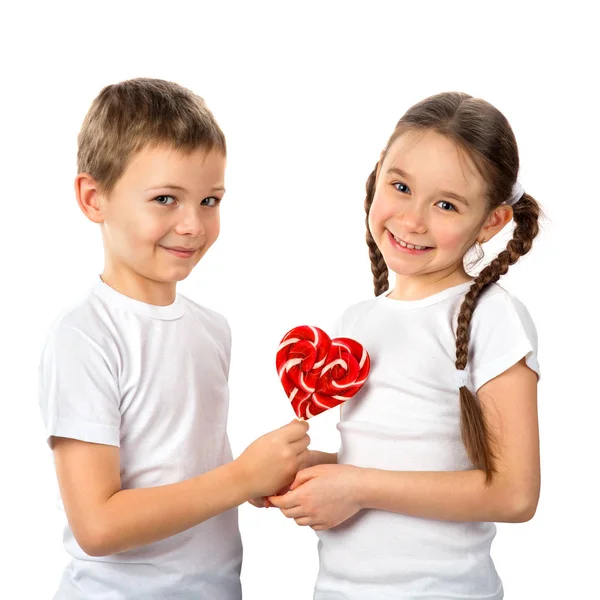 Junge schenkt einem kleinen Mädchen Süßigkeiten Lutscher Herz isoliert auf weiß. Valentinstag. Kinder lieben. — Stockfoto
