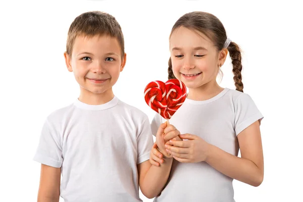 Junge schenkt einem kleinen Mädchen Süßigkeiten Lutscher Herz isoliert auf weiß. Valentinstag. Kinder lieben. — Stockfoto