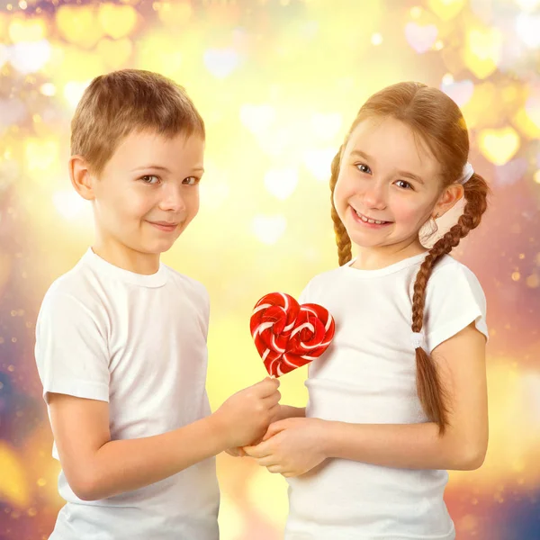 Junge schenkt einem kleinen Mädchen bonbonrote Lutscher in Herzform. Valentinstag Kunst Porträt. — Stockfoto