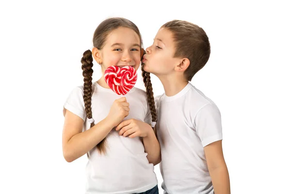 Niño besa niña con caramelo lollipop rojo en forma de corazón aislado en blanco —  Fotos de Stock
