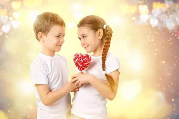 Boy le da a una niña caramelo lollipop rojo en forma de corazón. Día de San Valentín — Foto de Stock