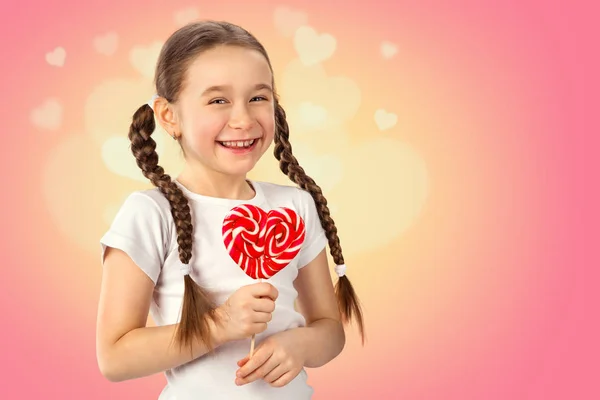 Söt liten flicka i kärlek med candy lollipop hjärta på rosa bakgrund. Alla hjärtans dag. — Stockfoto