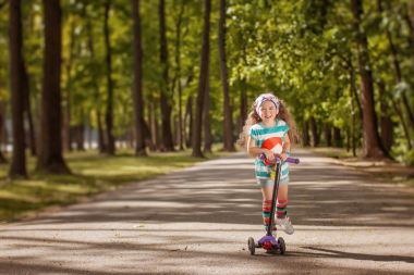 Küçük kız güneşli yaz gününde bir parkta scooter binmek öğrenmek.