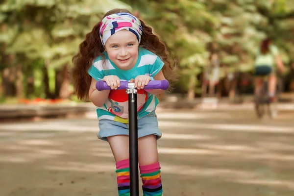 Niña aprender a montar scooter en un parque en el soleado día de verano . —  Fotos de Stock