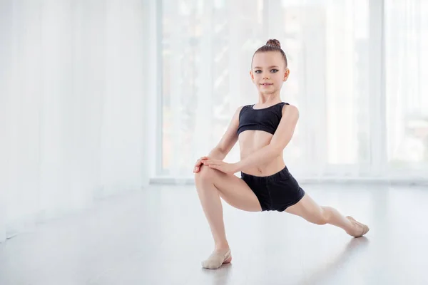 Flexible child, beautiful little gymnast girl doing gymnastic exercises or exercising in fitness class