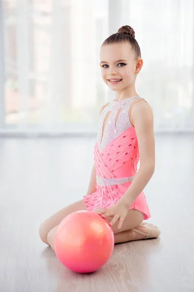 Hermosa niña gimnasta en vestido de ropa deportiva rosa, la realización de elemento de gimnasia de arte con pelota en la clase de fitness —  Fotos de Stock