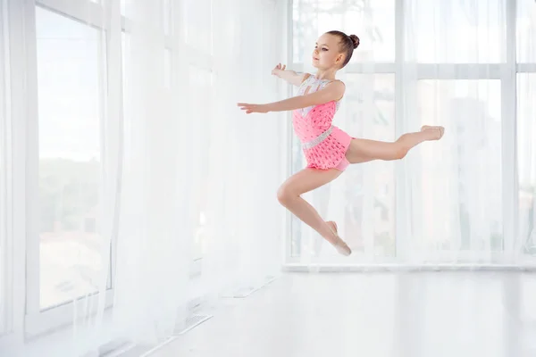 Menina ginasta em vestido de sportswear rosa, executando elemento de ginástica de arte, pulando, fazendo salto dividido no ar — Fotografia de Stock
