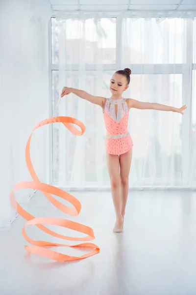 Schöne kleine Turnerin Mädchen in rosa Sportbekleidung Kleid, macht rhythmische Gymnastikübungen Spiralen mit Kunstband — Stockfoto