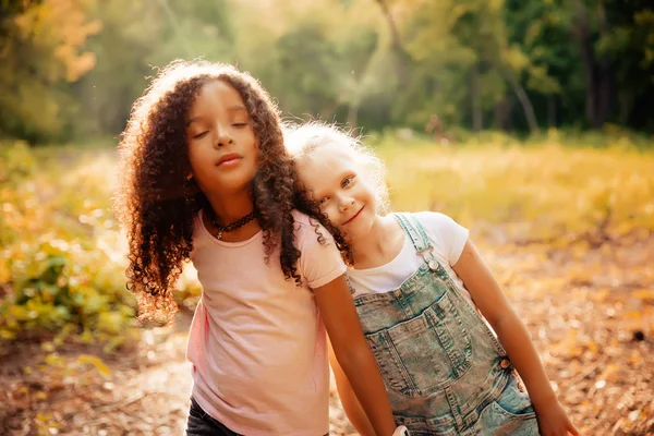 Twee gelukkige meisjes als vrienden omhelzen elkaar op vrolijke manier. Weinig vriendinnen in park. — Stockfoto