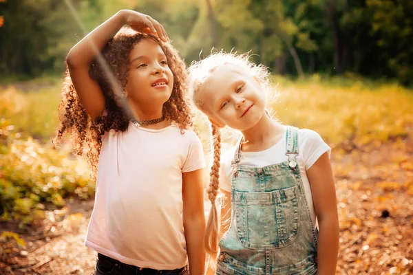 Twee gelukkige meisjes als vrienden omhelzen elkaar op vrolijke manier. Weinig vriendinnen in park. — Stockfoto