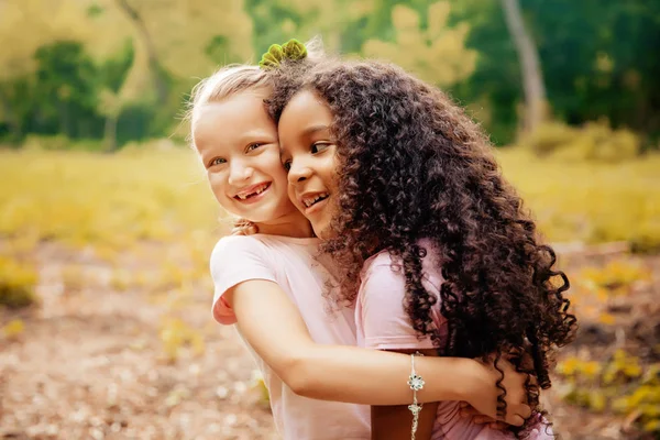 Dos chicas felices como amigas se abrazan de manera alegre. Pequeñas amigas en el parque . —  Fotos de Stock